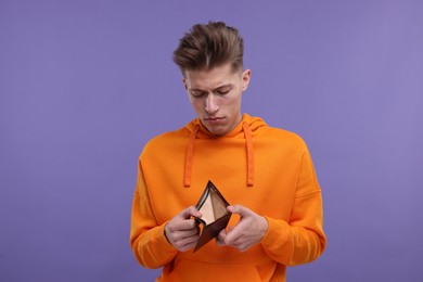 Upset man looking at his empty wallet on purple background