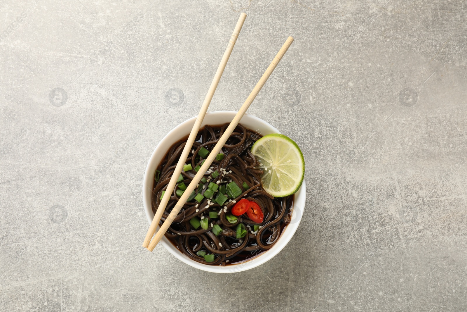 Photo of Tasty buckwheat noodles (soba) with sauce, onion in bowl and chopsticks on light grey table, top view