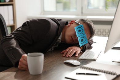 Photo of Man with fake eyes painted on sticky notes snoozing at workplace in office