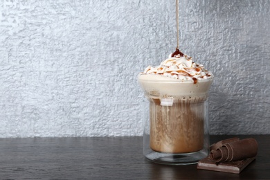 Pouring sweet syrup into glass cup with tasty coffee on wooden table. Space for text