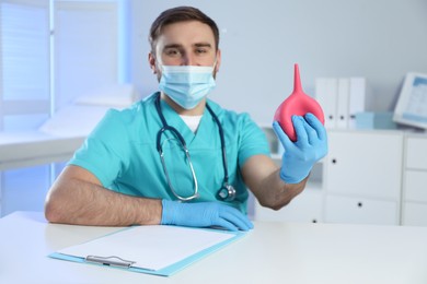 Photo of Doctor holding rubber enema at table in examination room, focus on hand
