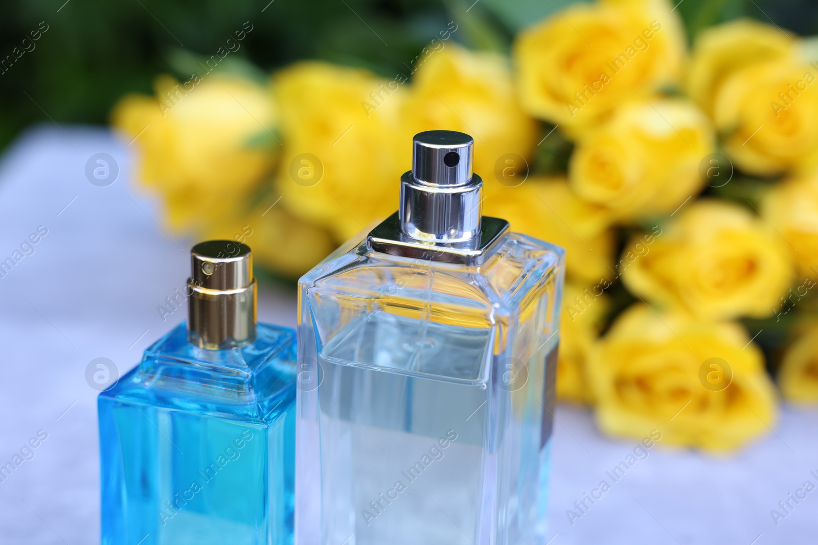 Photo of Perfumes and beautiful bouquet of yellow roses on light table, selective focus