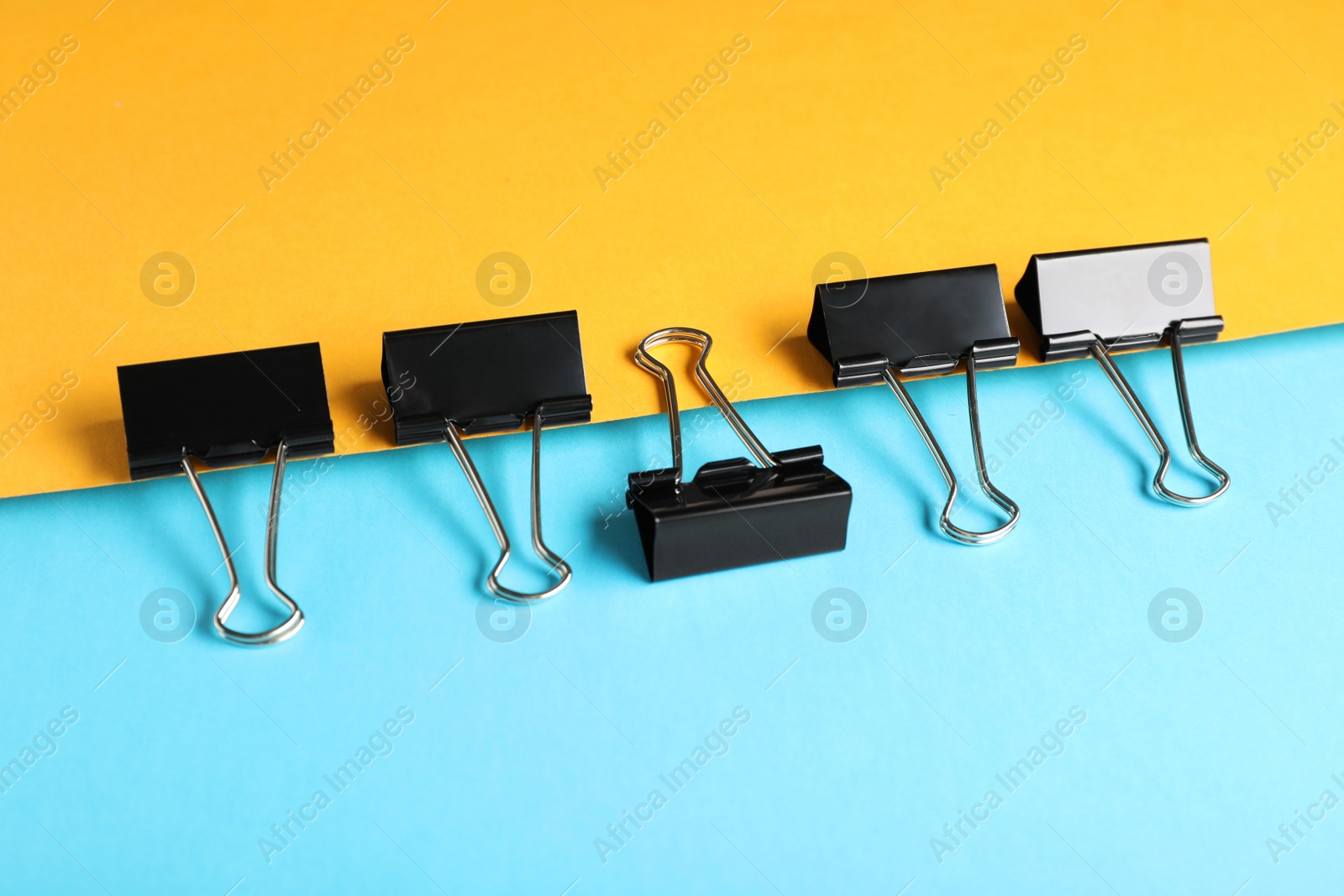 Photo of Black binder clips on color background. Stationery items