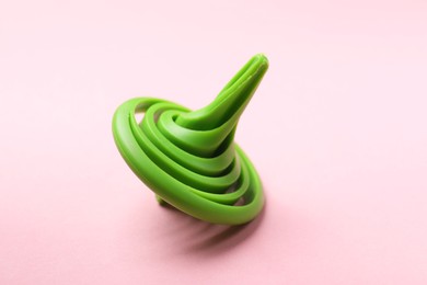 Photo of One green spinning top on pink background, closeup