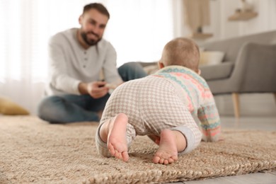 Photo of Happy young father watching his cute baby crawl on floor at home