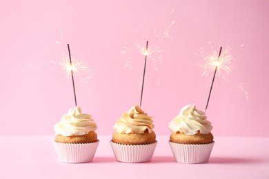 Photo of Delicious birthday cupcakes with burning sparklers on color background