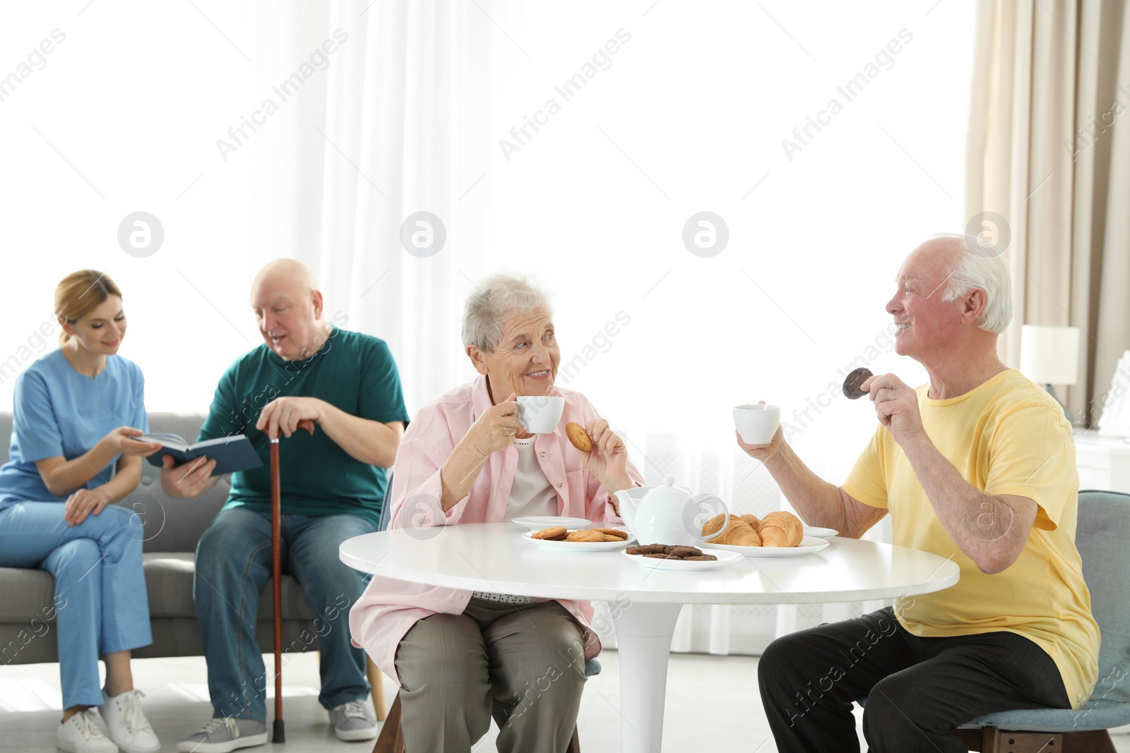 Photo of Nurse assisting elderly man while senior couple having breakfast at retirement home