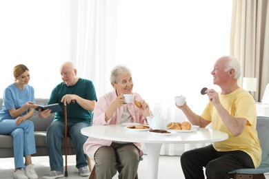 Photo of Nurse assisting elderly man while senior couple having breakfast at retirement home
