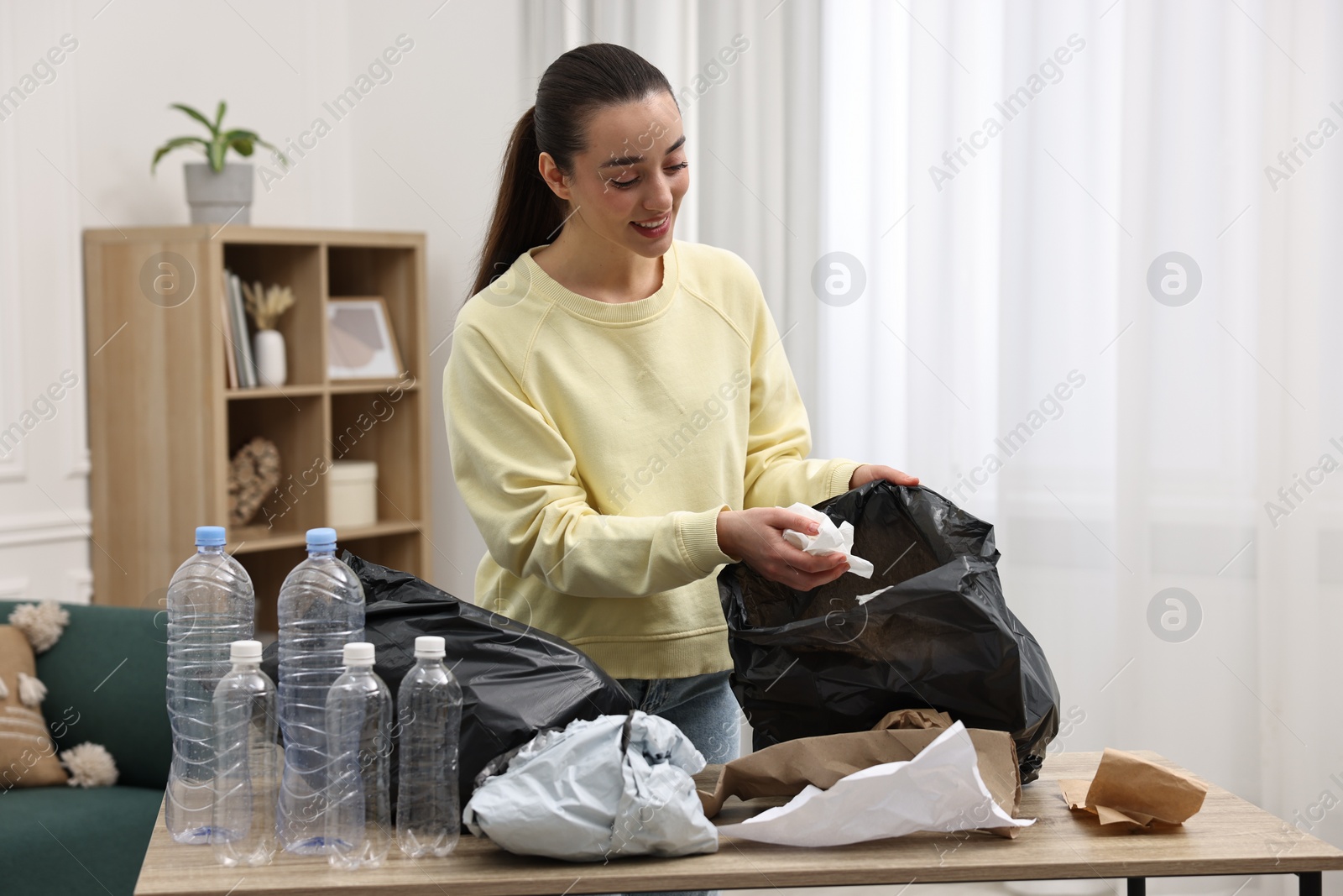 Photo of Smiling woman with plastic bag separating garbage in room