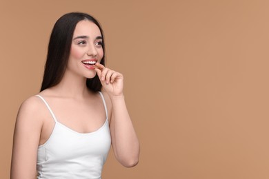 Beautiful young woman with vitamin pill on beige background. Space for text