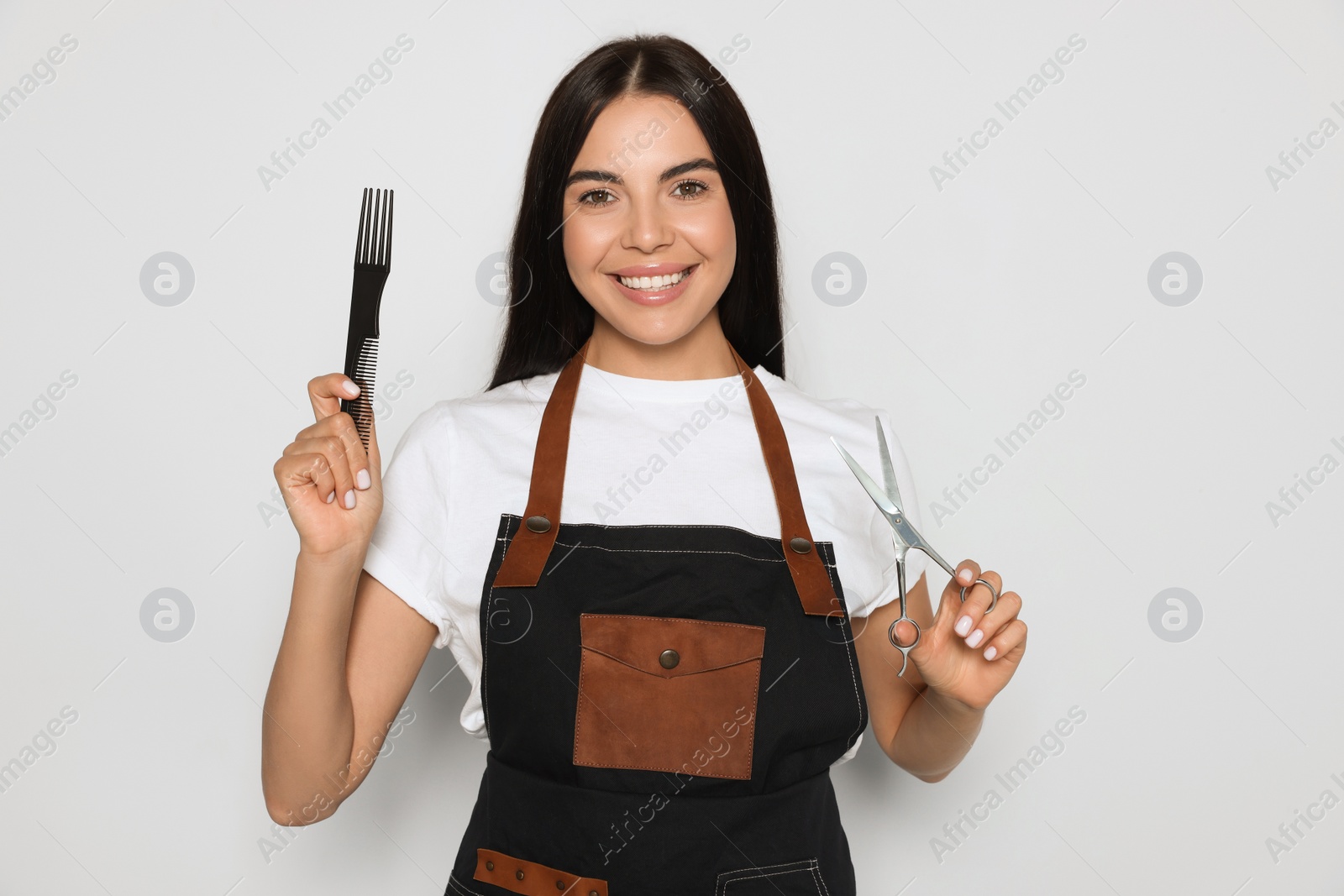 Photo of Portrait of happy hairdresser with professional scissors and comb on light background