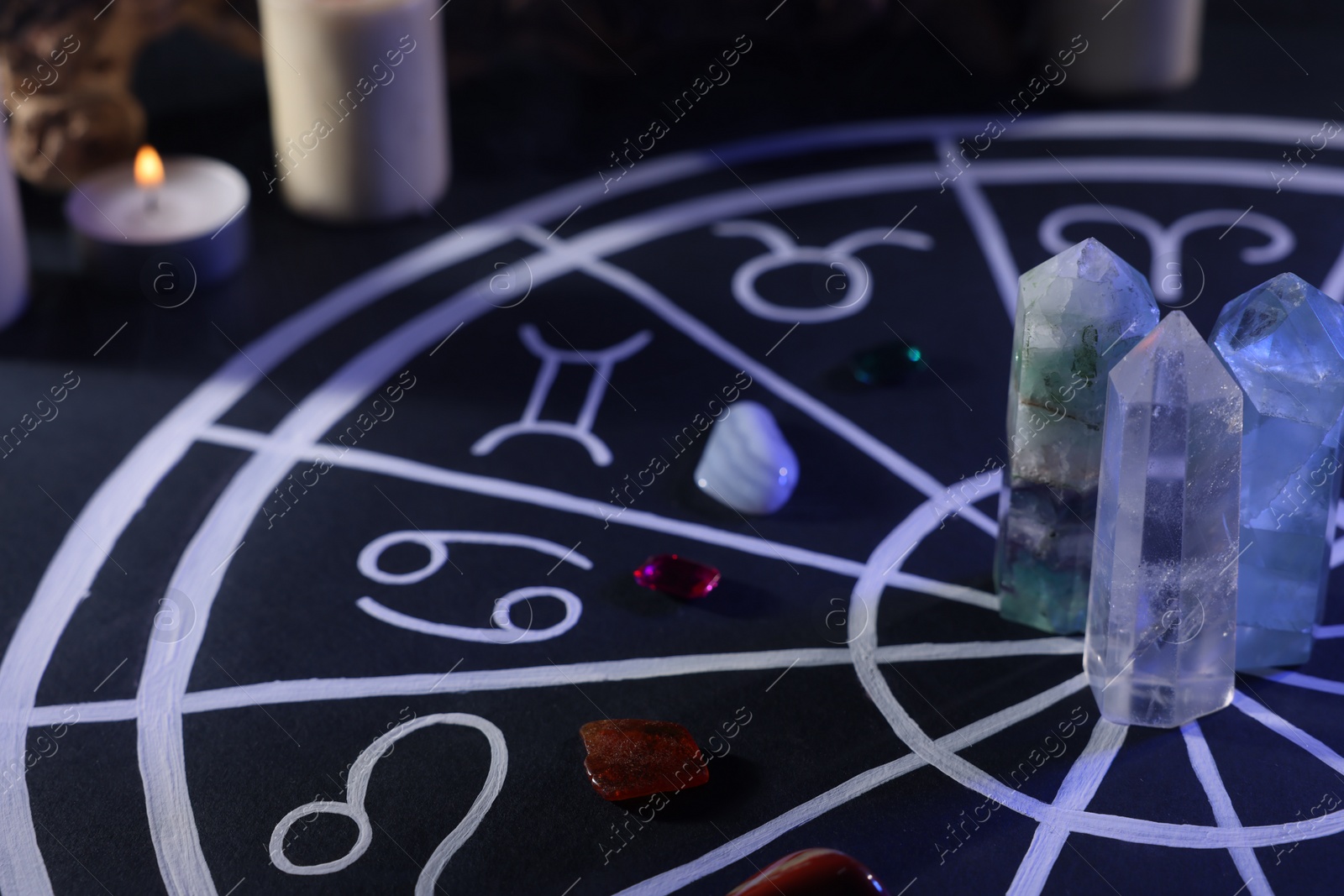 Photo of Natural stones for zodiac signs, drawn astrology chart and burning candle on black table, closeup