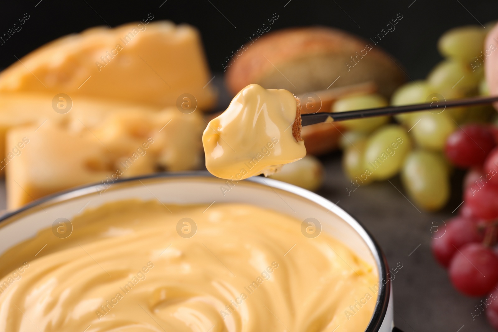 Photo of Piece of bread over pot with delicious cheese fondue, closeup