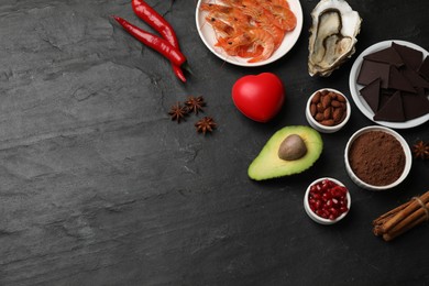 Photo of Natural aphrodisiac. Different food products and heart model on black table, flat lay. Space for text