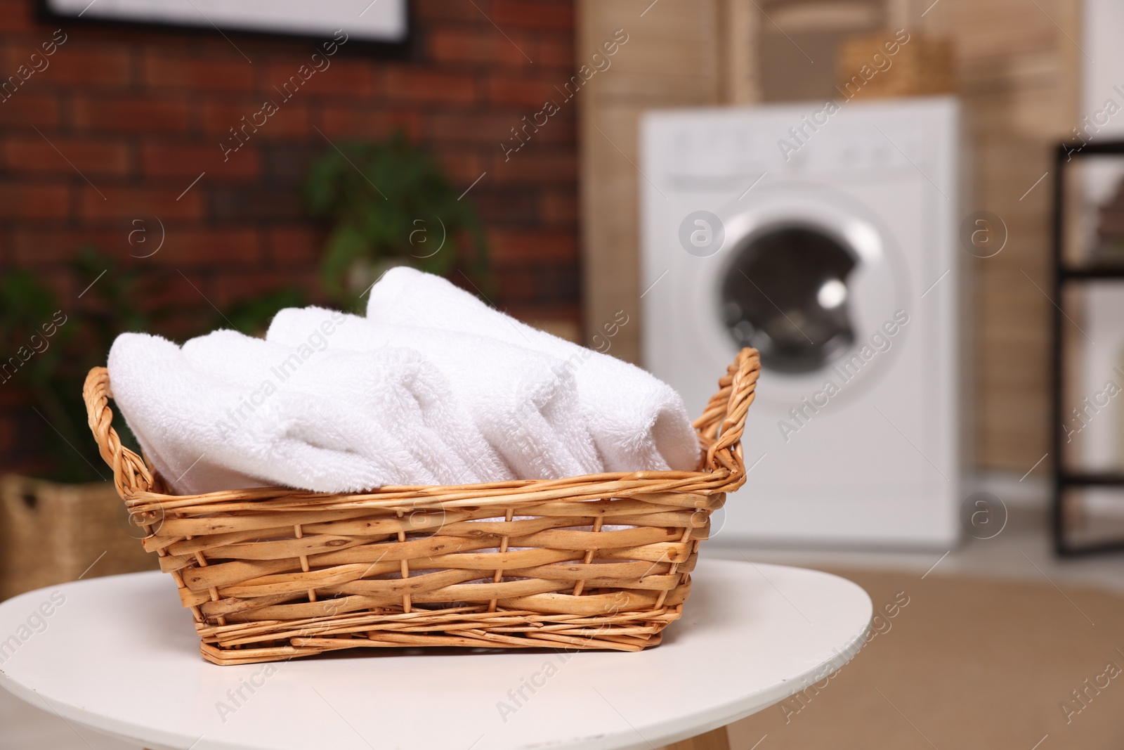 Photo of Wicker basket with folded towels on white table in laundry room