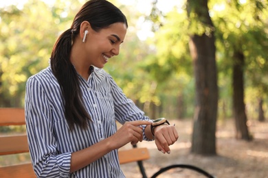 Photo of Young woman with wireless earphones and smart watch in park