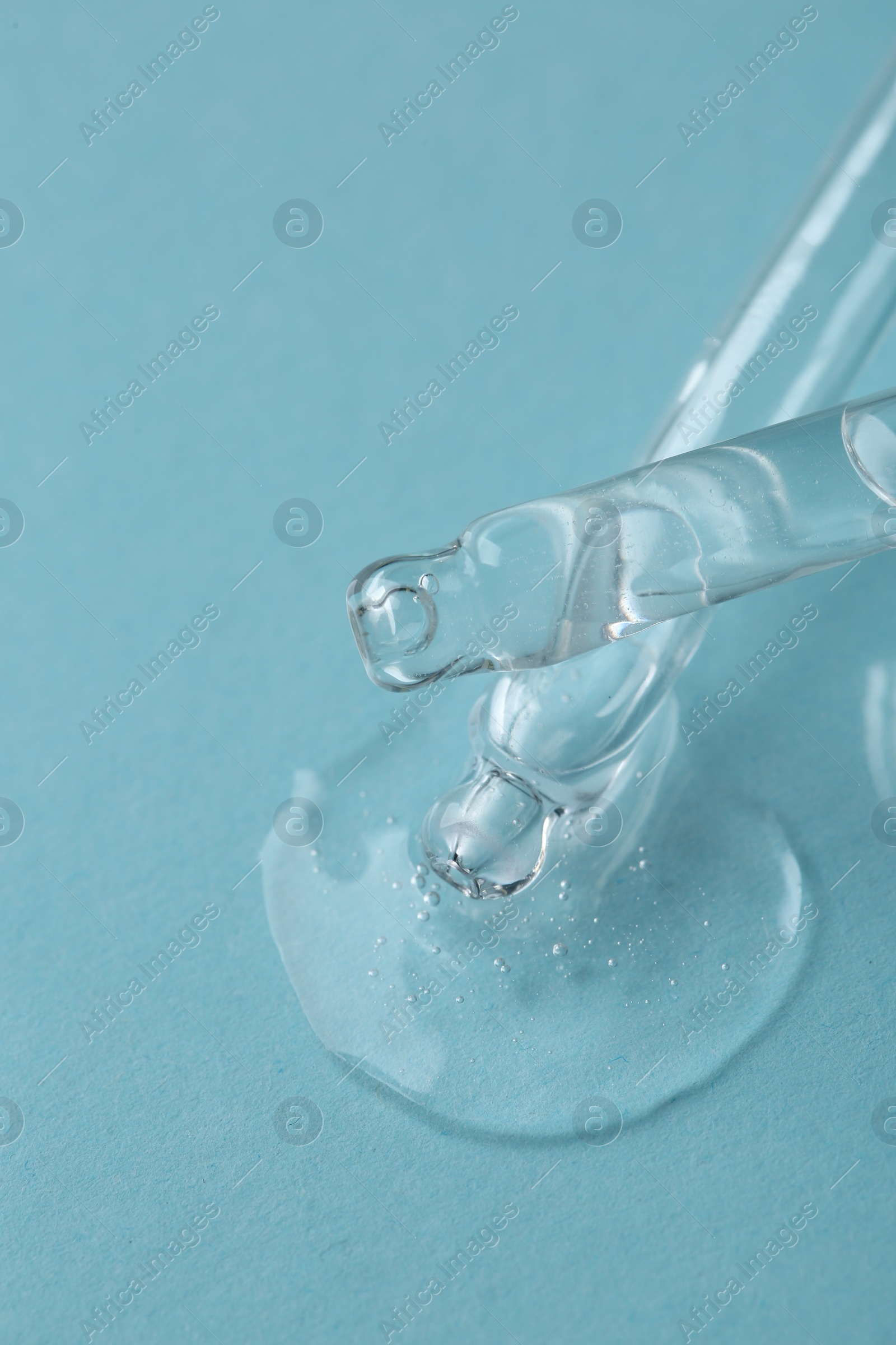Photo of Dripping cosmetic serum from pipettes onto light blue background, macro view
