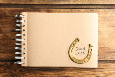 Notebook with phrase GOOD LUCK and horseshoe on wooden table, top view. Space for text