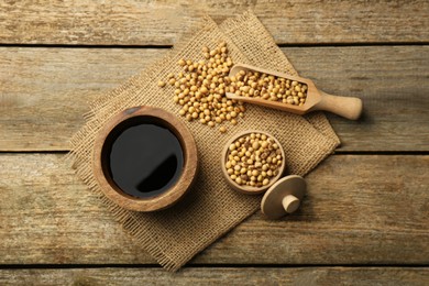 Photo of Soy sauce in bowl and soybeans on wooden table, flat lay