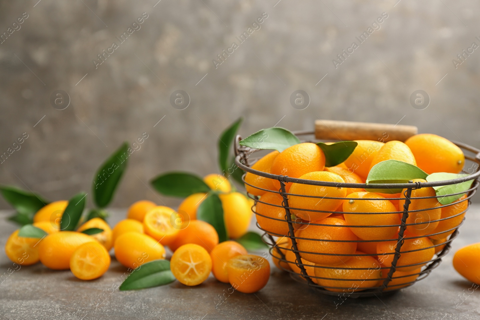 Photo of Fresh ripe kumquats in bowl on grey table, space for text