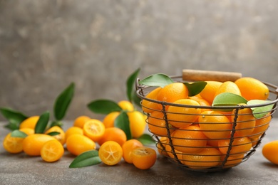 Photo of Fresh ripe kumquats in bowl on grey table, space for text