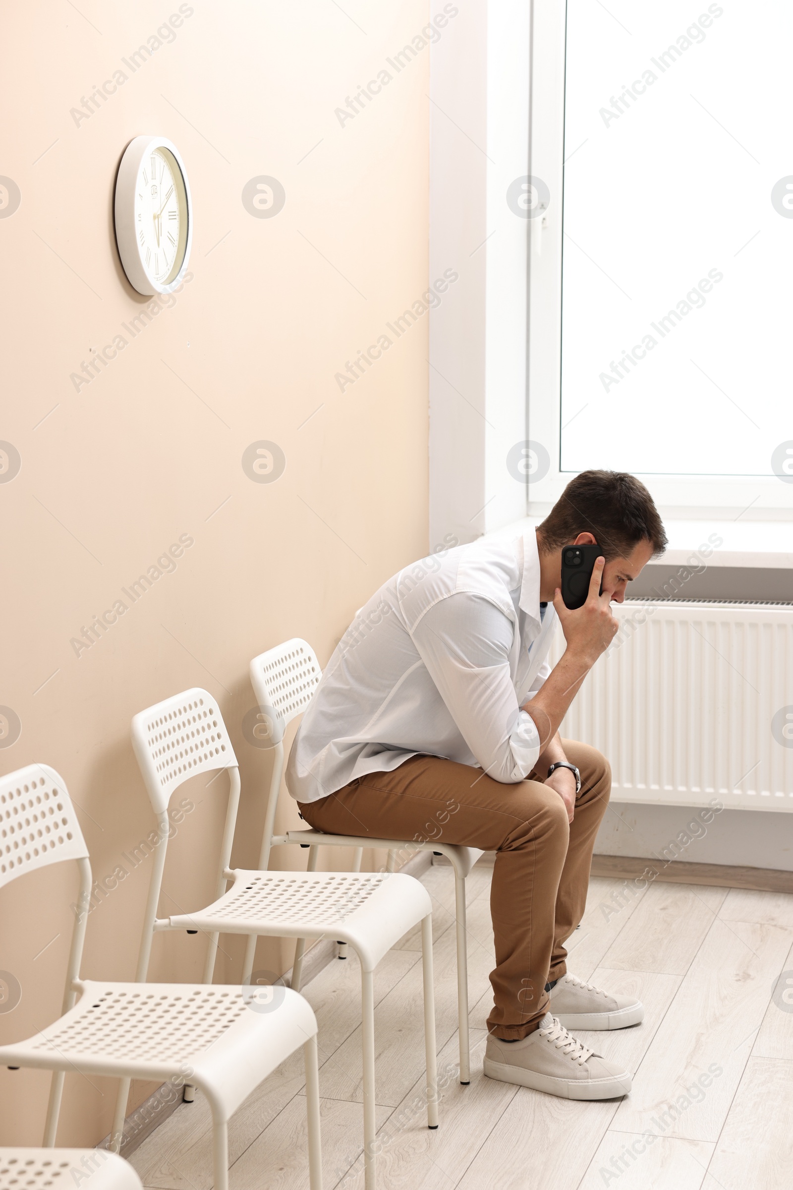 Photo of Man talking on smartphone and waiting for appointment indoors