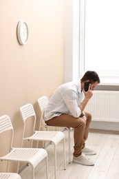 Man talking on smartphone and waiting for appointment indoors