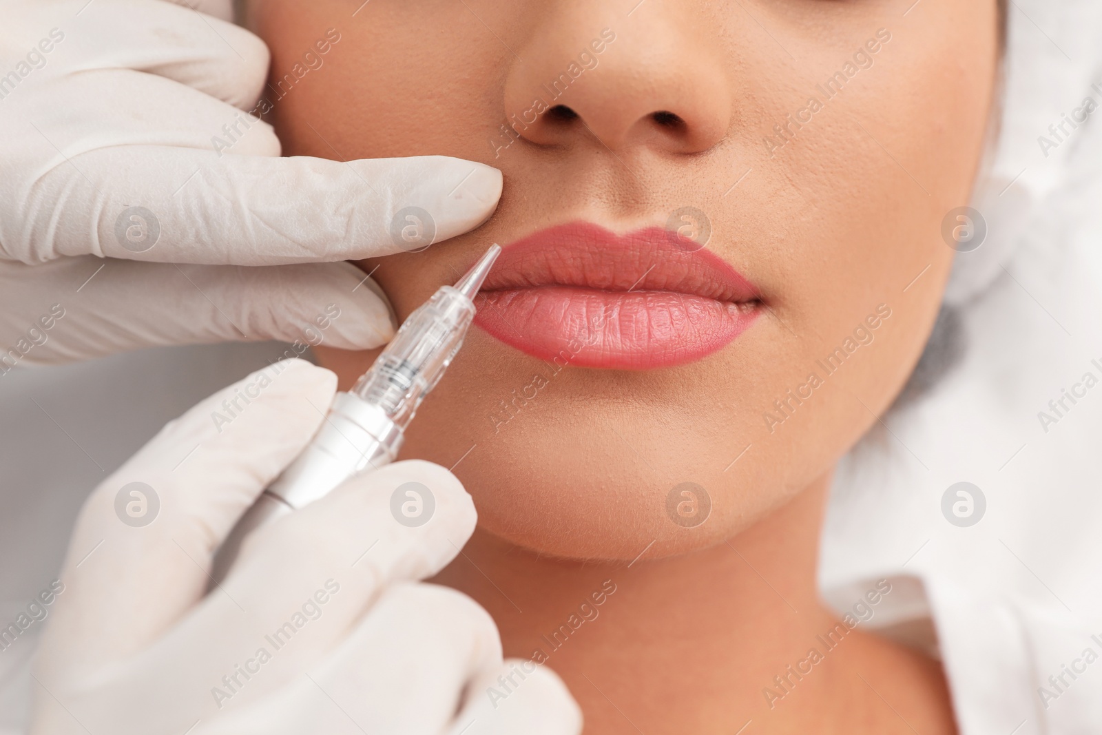 Photo of Young woman undergoing procedure of permanent lip makeup in tattoo salon, closeup