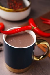 Cup of hot chocolate with chili pepper on grey table