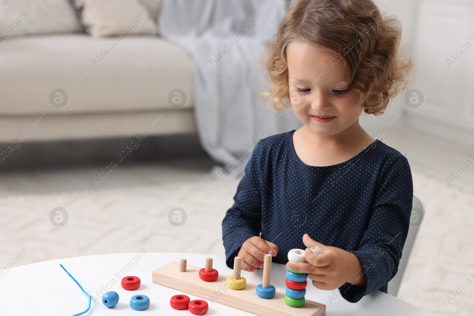 Photo of Motor skills development. Little girl playing with stacking and counting game at table indoors