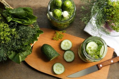 Glass jars, fresh cucumbers and herbs on wooden table, flat lay. Pickling recipe