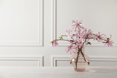 Magnolia tree branches with beautiful flowers in glass vase on white wooden table, space for text