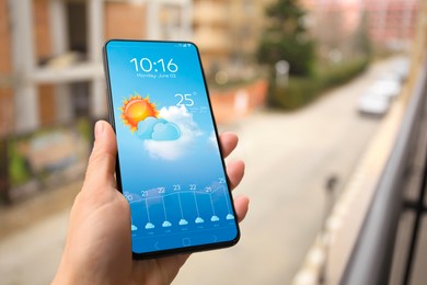 Woman checking weather using app on smartphone outdoors, closeup. Data and illustration of sun with cloud on screen
