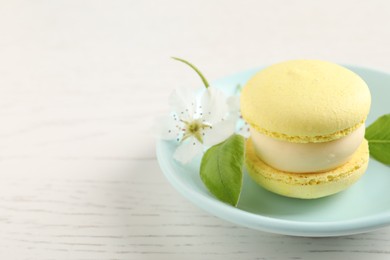 Delicious yellow macaron and flower on white wooden table, closeup. Space for text