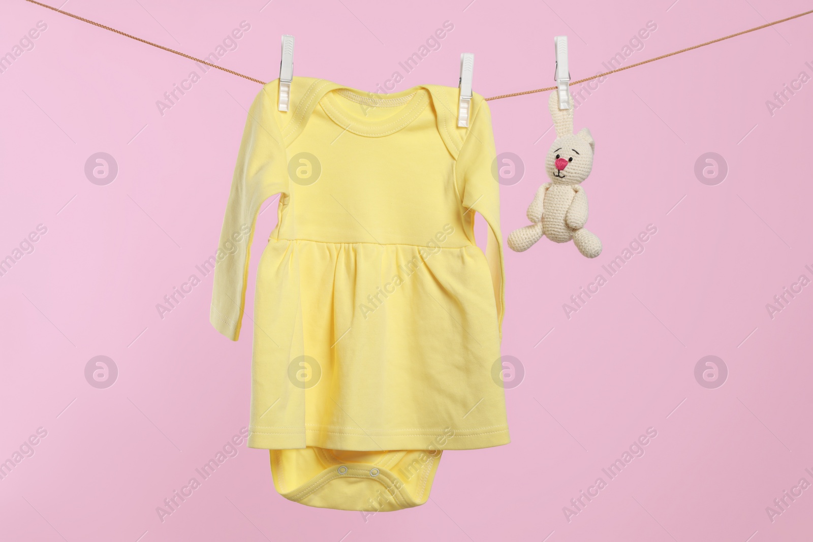 Photo of Yellow baby dress and crochet toy drying on washing line against pink background