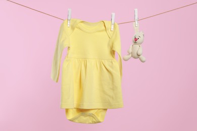 Yellow baby dress and crochet toy drying on washing line against pink background