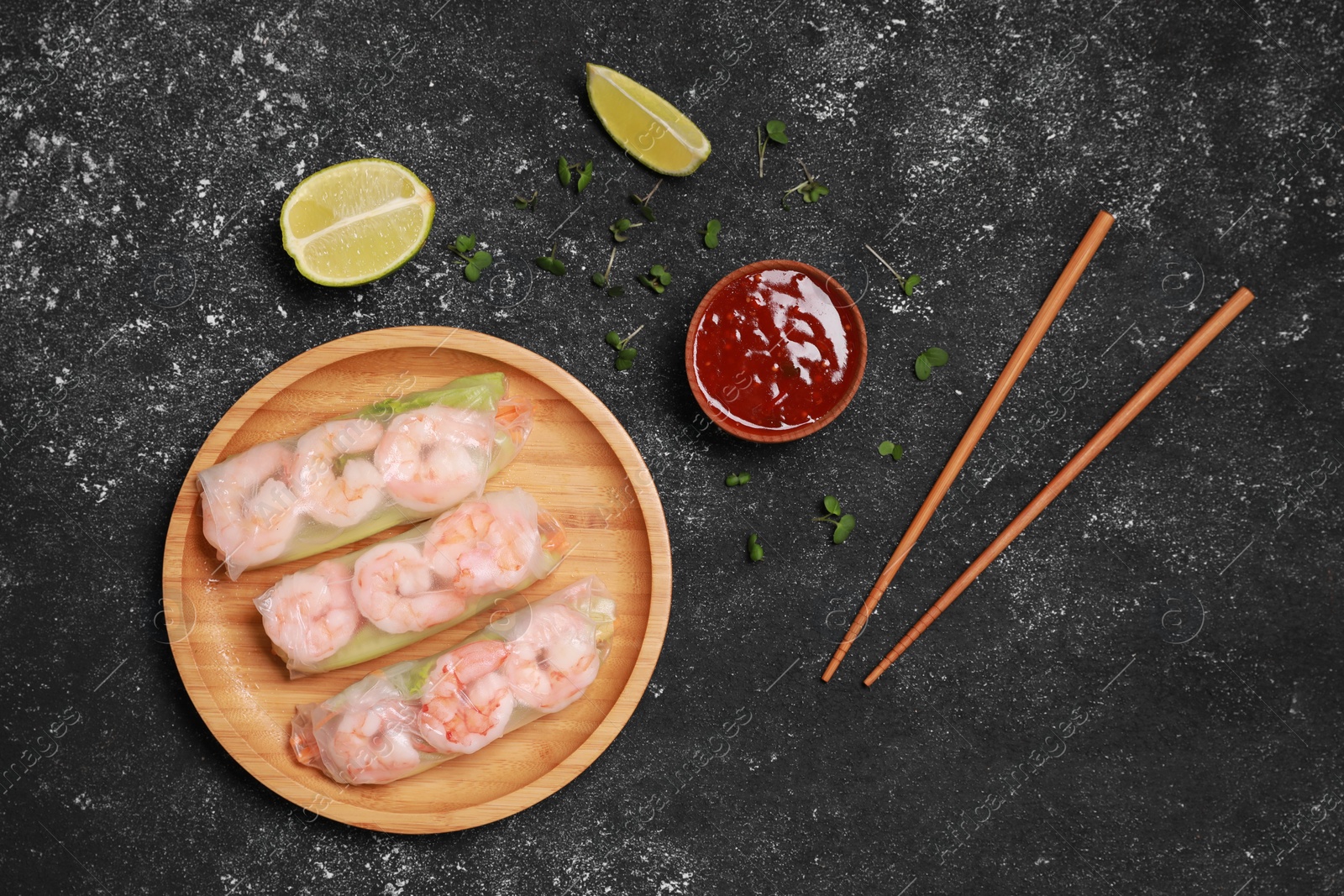 Photo of Tasty spring rolls, chopsticks, sauce, sliced lime and microgreens on grey textured table, flat lay