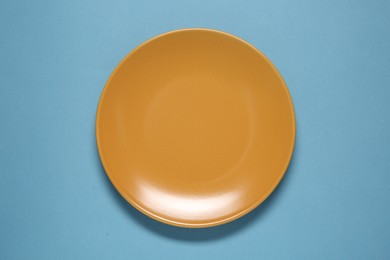 Photo of One orange ceramic plate on light blue background, top view