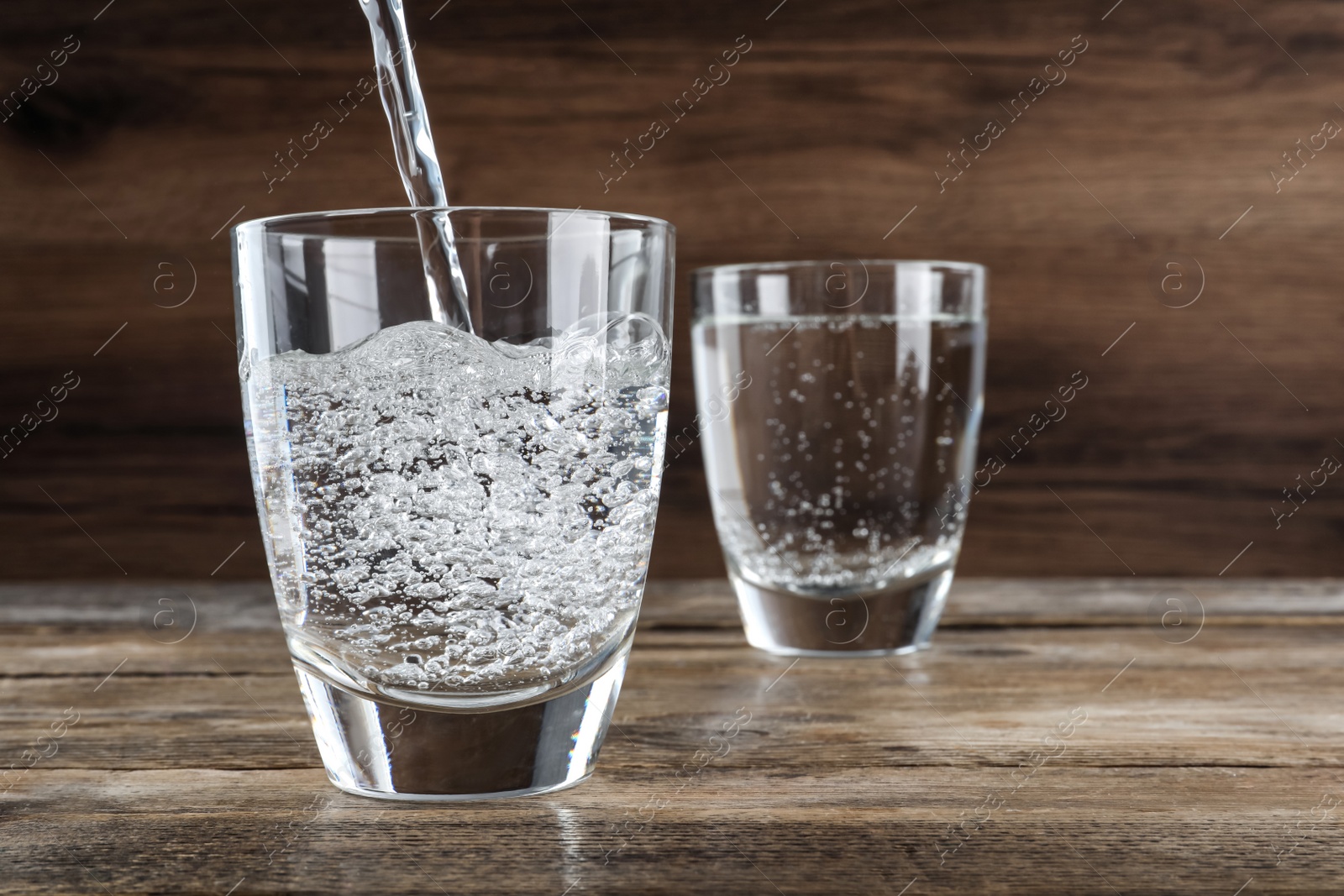 Photo of Pouring soda water into glass on wooden table. Space for text