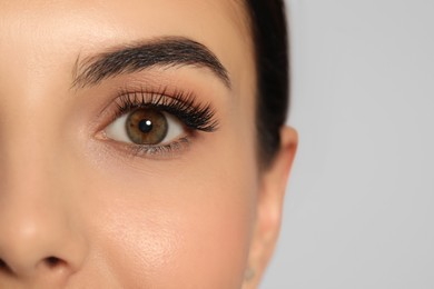 Beautiful young woman with long eyelashes on light background, closeup