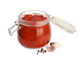Photo of Glass jar of delicious canned lecho, garlic and peppercorns on white background