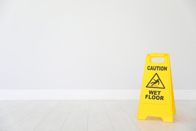 Photo of Safety sign with phrase "CAUTION WET FLOOR" on floor near light wall