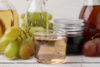 Photo of Different types of vinegar and grapes on wooden table, closeup