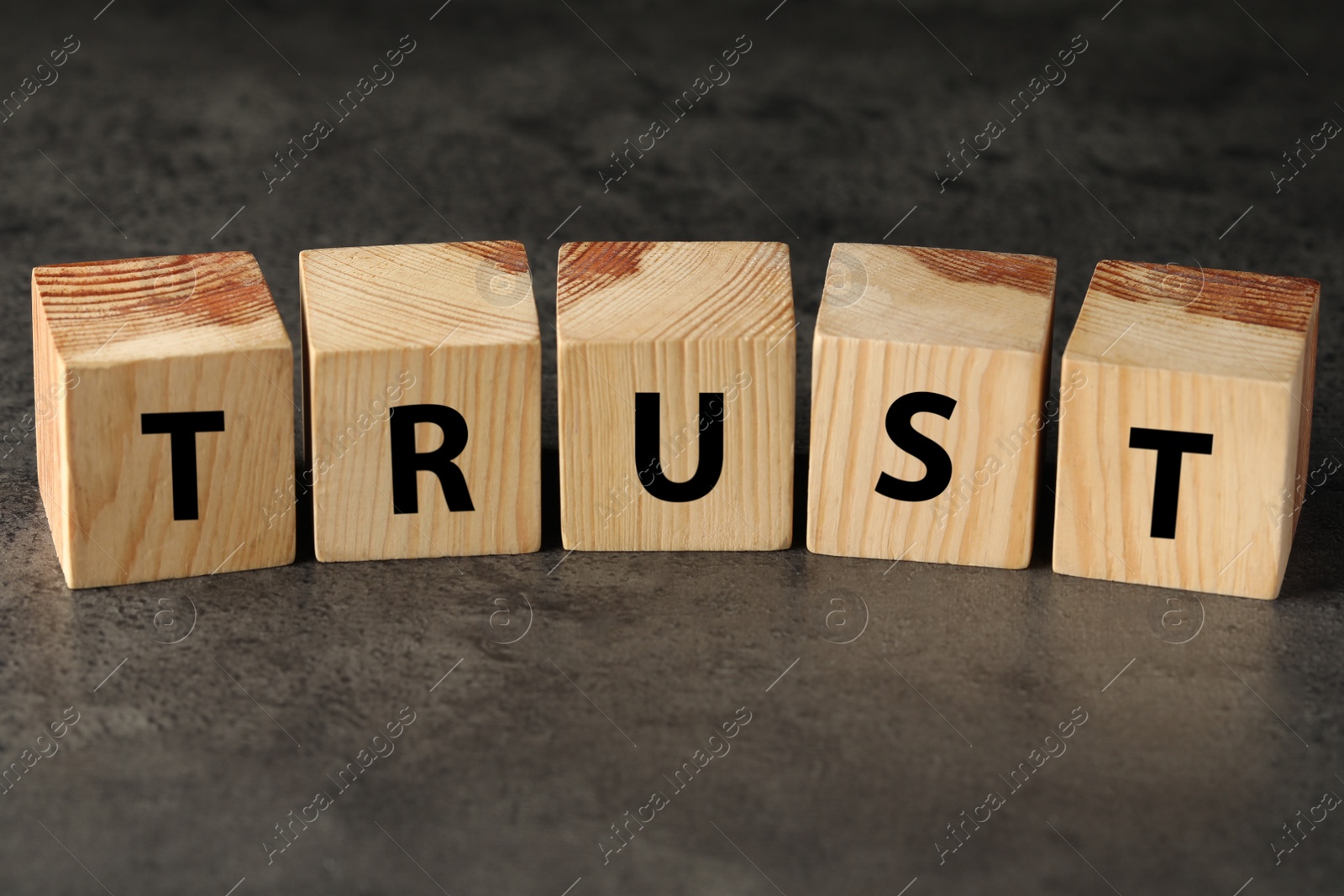 Photo of Word TRUST made with wooden cubes on grey table, closeup