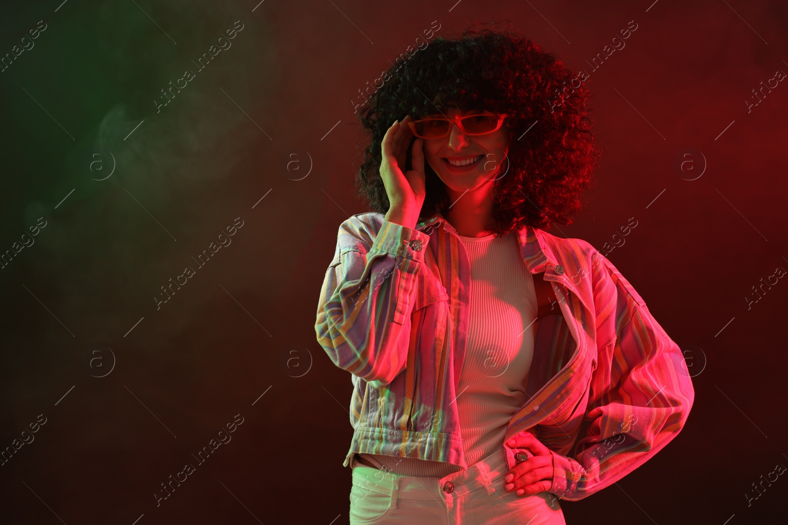 Photo of Beautiful young woman in sunglasses posing on color background in neon lights. Space for text