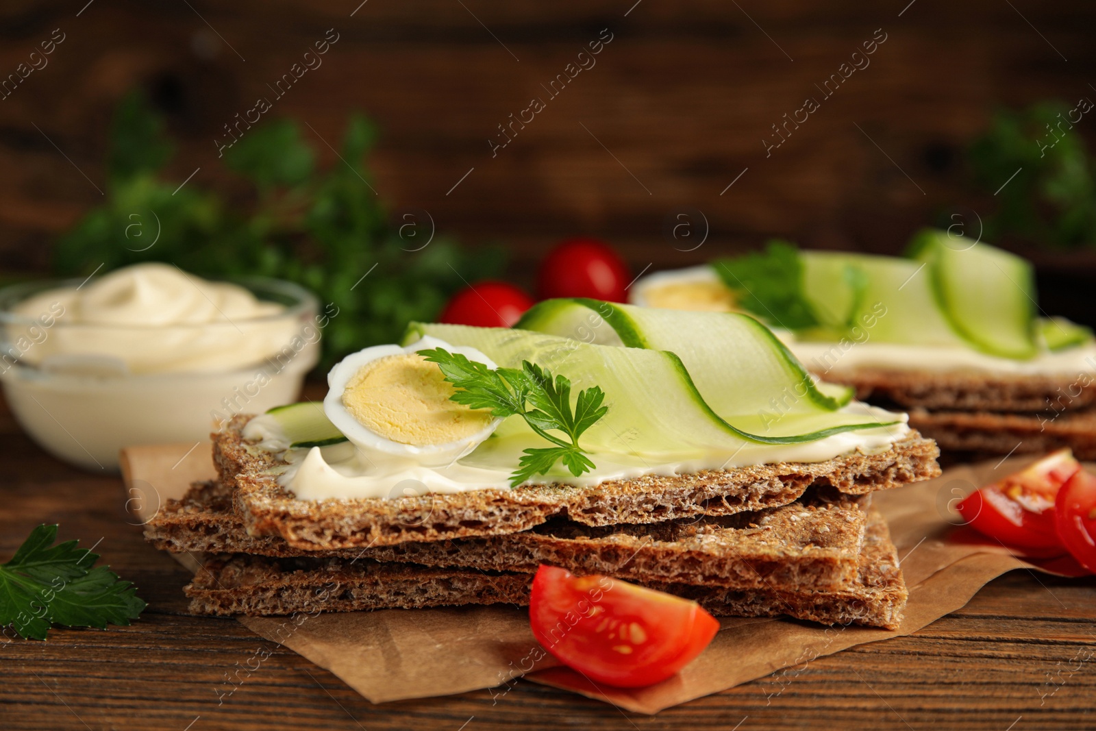 Photo of Fresh rye crispbreads with quail egg, cream cheese and cucumber slices on wooden table, closeup