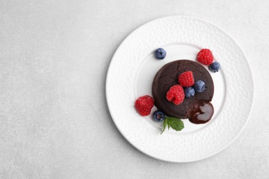 Plate with delicious chocolate fondant, berries and mint on light grey table, top view. Space for text