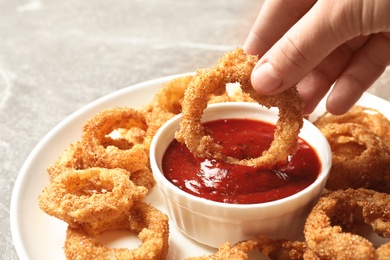 Photo of Woman dipping crunchy fried onion ring in tomato sauce, closeup