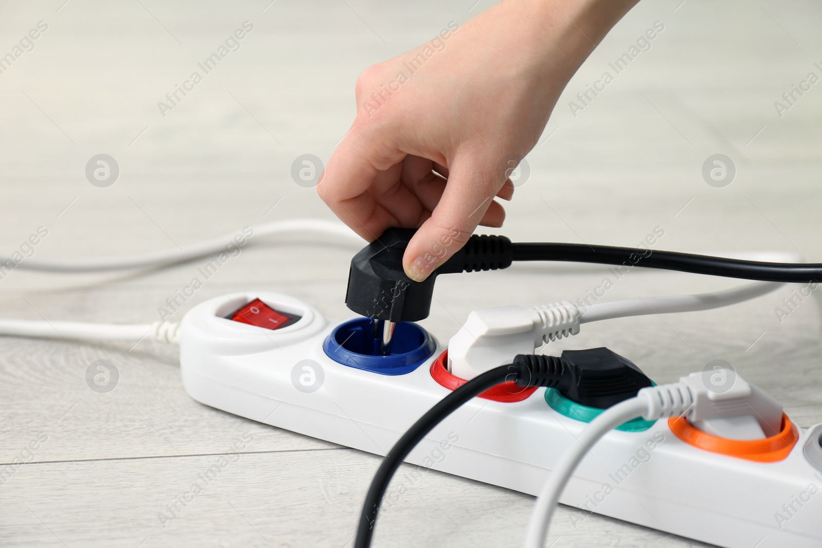 Photo of Woman inserting power plug into extension cord on floor, closeup. Electrician's professional equipment