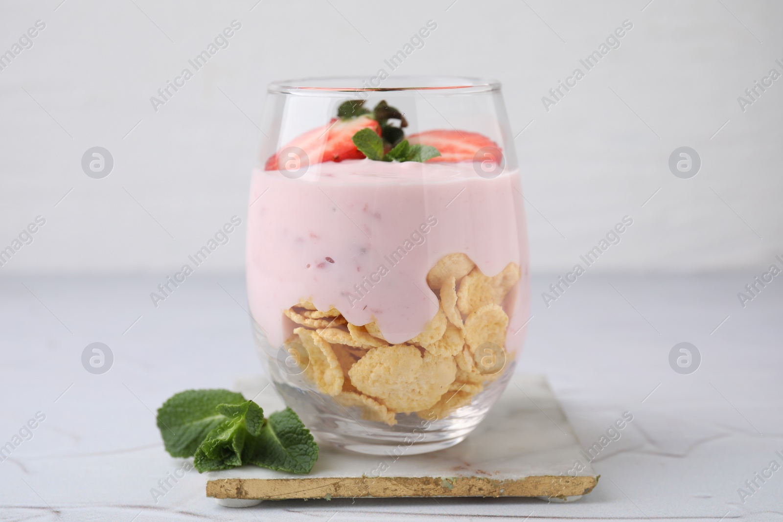 Photo of Glass with yogurt, strawberries and corn flakes on white textured table